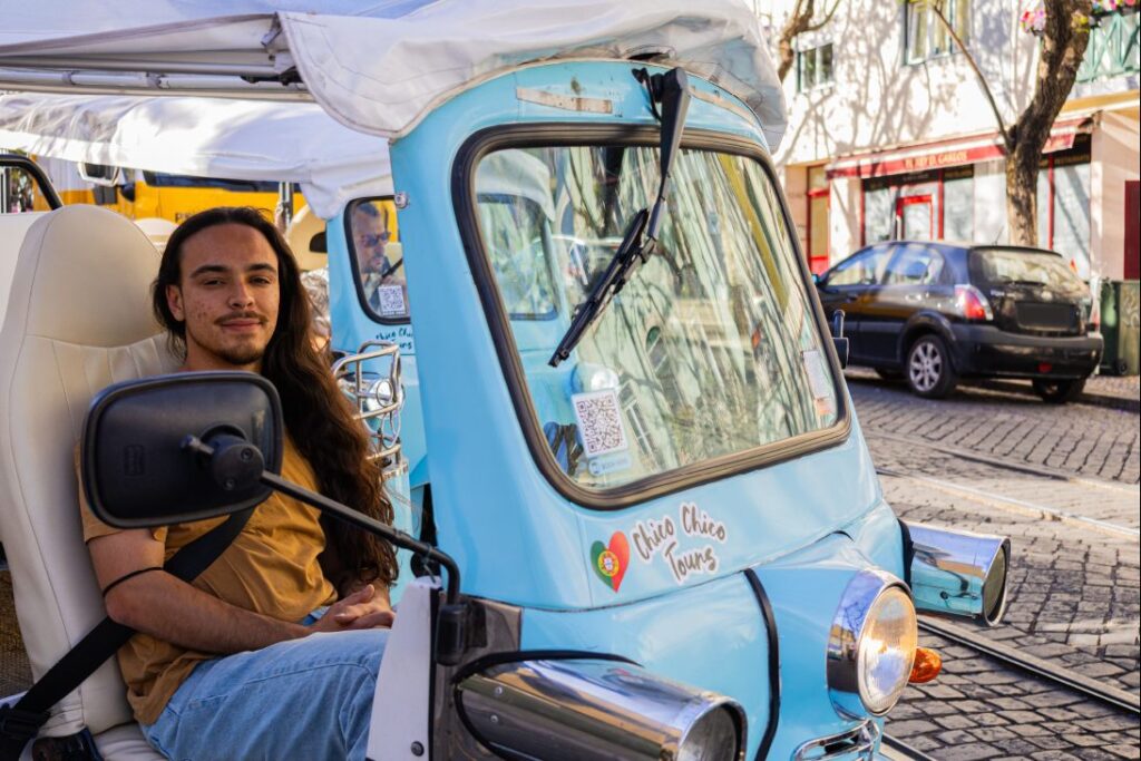 A Chico Chico Tours guide smiling at the wheel of a light blue electric tuk-tuk