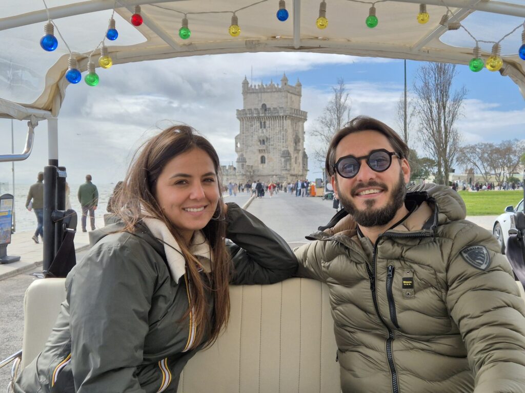 Guests smiling in a Chico Chico tuk-tuk in front of Belem Tower