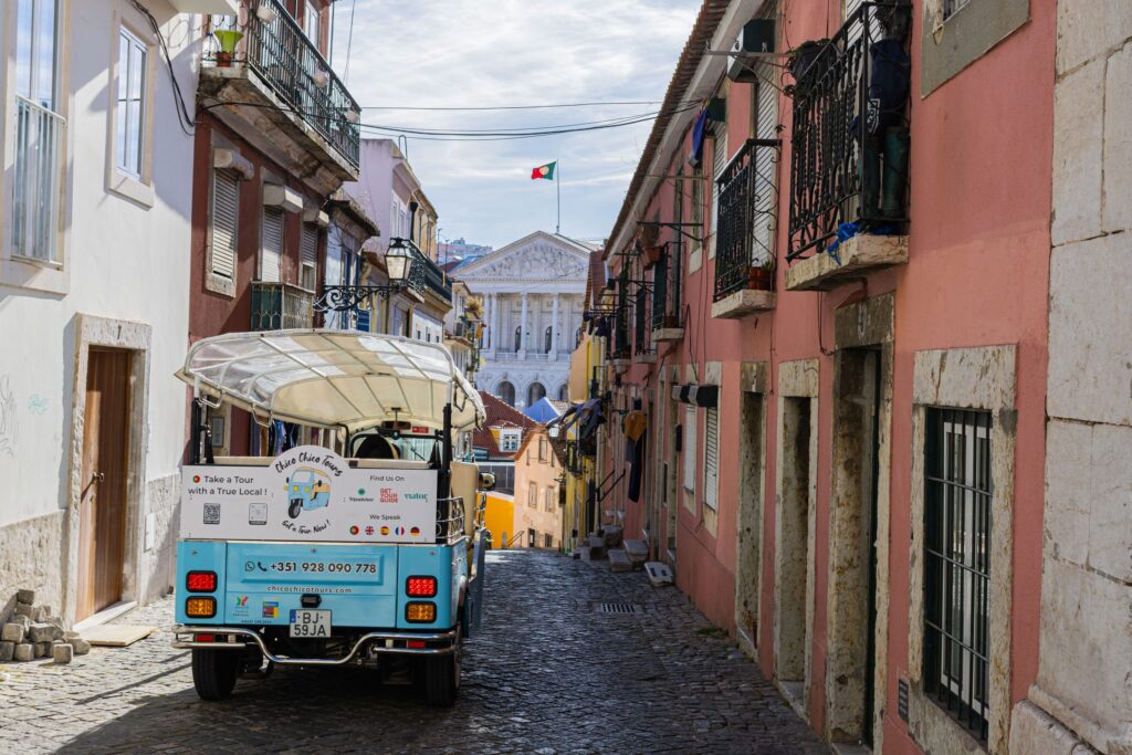 Chico Chico tuk-tuk in a narrow Lisbon street with the Parliament behind