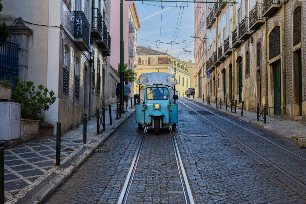 A light blue tuk-tuk on a narrow street between pastel buildings in Lisbon